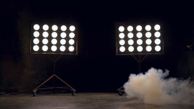 Black large room of color with working searchlights spotlights. The smoke in the lower left corner begins to go. cold theatrical smoke machine 4k
