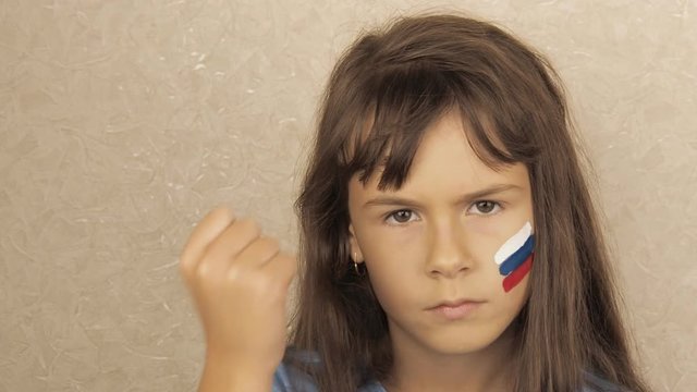A little girl with a flag of russia on her face shows a fist.