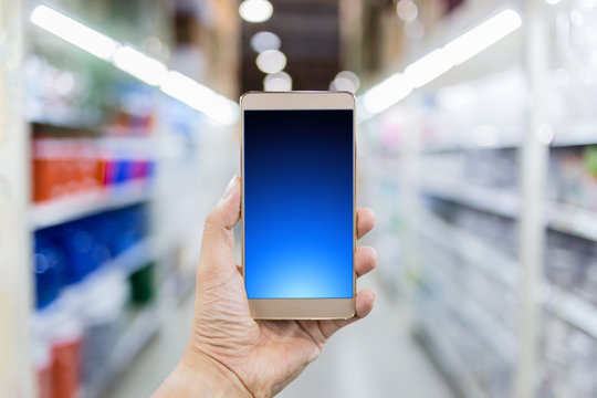 hand with smartphone and blur image background of shelf in supermarket shop