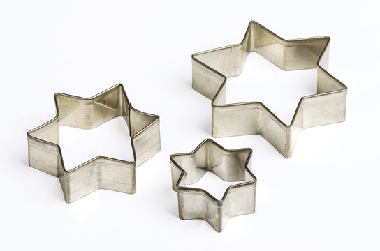 Three star shaped Christmas cookie cutters over white. Tin biscuit cutters, tool to cut cookie dough in particular shapes and to make cutouts. Hexagram shaped and six pointed geometric star figures.