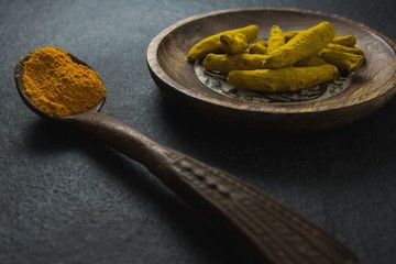 Turmeric powder in spoon and turmeric sticks in plate