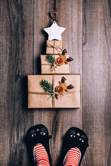 Three brown paper wrapped gifts laid out in the shape of a Christmas tree with star on top. Woman...