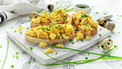 Homemade Quail Scrambled eggs on crispy toast, bread with green onion, chives on white board.