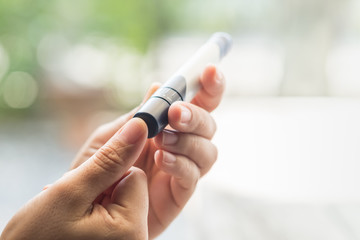 Close up of woman hands using lancet on finger to check blood sugar level by Glucose meter using as Medicine, diabetes, glycemia, health care and people concept.