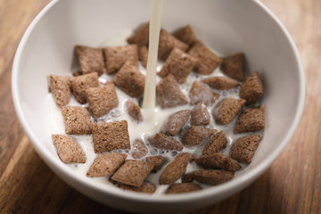 pouring milk into chcolate cereal pillow in white bowl on table