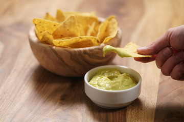 young female hand dipping nachos in guacamole sauce
