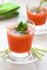 Tomato juice with parsley and celery greens in a glass on a saucer, with a green napkin, with a blurry background.
