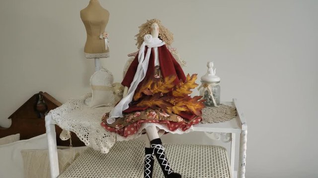 A beautiful doll sits on a shelf with a maple branch.