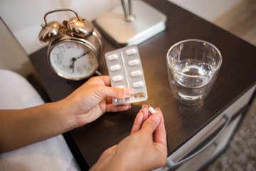 Woman taking medicine pills in the bedroom