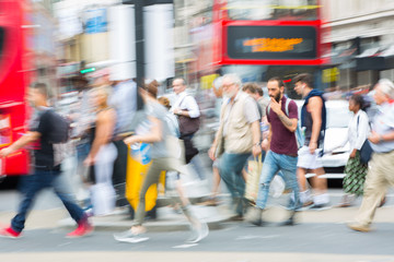 Piccadilly circus with lots of people, tourists and Londoners crossing the junction. Red bus at the background. Blurred type image. London, UK