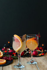 Vertical photo of winter lemonade with grapefruit slices, red currant berries and cinamon sticks in wine glasses, black board and christmas lights on background
