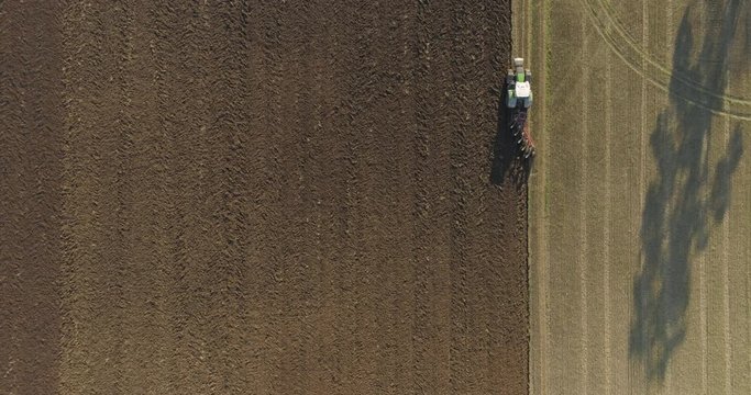 teady top down aerial footage of tractor plowing field. Farmer cultivating arable land for seeding. Top view of soil plowing.