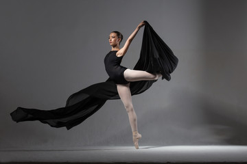 Graceful ballerina in black tights posing with black cloth