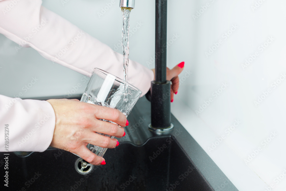 Wall mural Pouring water into a glass. The woman is tapping the tap water is running water. The glass is filled with water. Thirst, lack of water, global water problem.