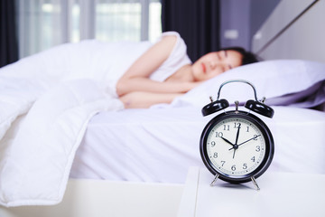 alarm clock on table and woman sleeping on bed in bedroom