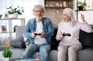 Cheerful senior married couple playing console together