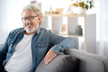 Joyful senior man sitting on sofa at home