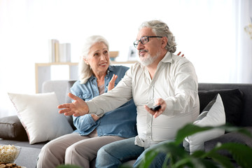 Senior husband and wife entertaining with television in living room