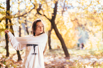 Young gorgeous woman stretching and warming up at park or forest. Attractive girl stretching before fitness in the autumn park.