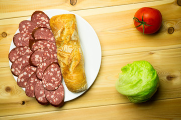 Sliced sausage on a white plate with bread on a wooden backgroun