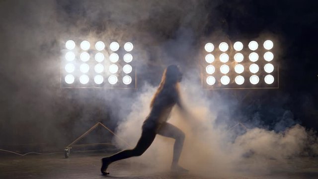 a young woman of pleasant appearance dances in the training hall in the lighting of searchlights in the background. a professional dance girl performs the set number in the style of lacquering and