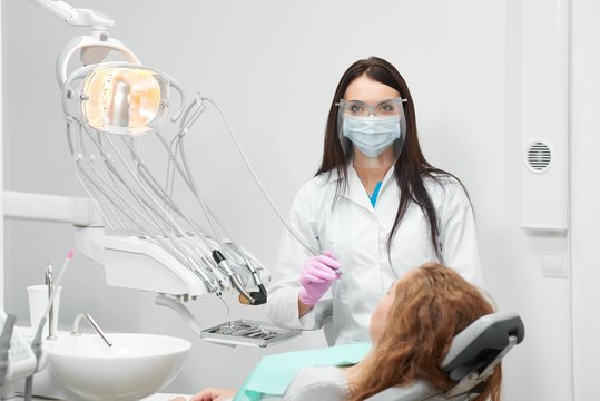 Professional female dentist wearing protective mask working at her clinic preparing to examine teethof her patient copyspace equipment technology medical tools hygiene healthcare medicine.