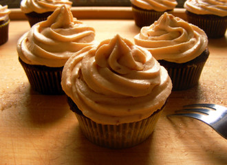 Cute chocolate cupcakes with crunchy peanut butter frosting on a wooden tray with a fork.