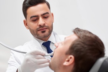 Fototapeta premium Handsome mature dentist concentrating while examining teeth of his male patient working at his clinic occupation confidence experience skilled profession dentistry concept.