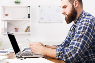 Obraz premium Young businessman in office using cell phone by the laptop