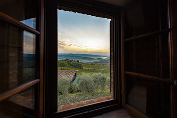 View through a window to a sunrise over foggy hills in Tuscany