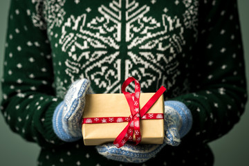 Christmas background. Girl is holding a Christmas present. Gifts for men. Merry Christmas. Gift for a girl. Sweater with Christmas ornament. Knitted dress. Box with gifts. Image in a dark key.