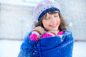 Winter portrait of a young woman.  Joyous Model Girl touching her face skin and laughing, having fun in the winter park. Beautiful young woman laughing outdoors. Enjoying nature, in winter and snow