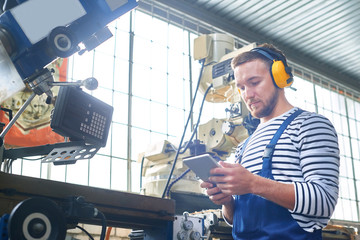 Portrait of young factory worker operating machine units at modern factory using digital tablet with electronic control, copy space