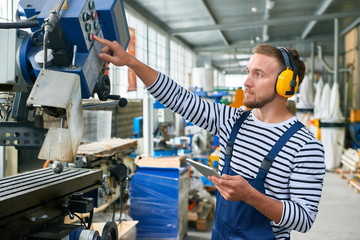 Side view portrait of young man pressing buttons on control panel while using metalworking machine...