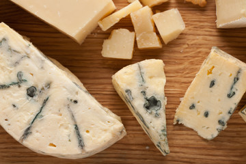 Tasting cheese dish on a wooden plate. Food for wine and romantic, cheese delicatessen on a dark stone table. Top view