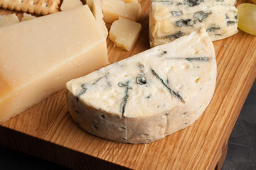 Tasting cheese dish on a wooden plate. Food for wine and romantic, cheese delicatessen on a dark stone table. Top view