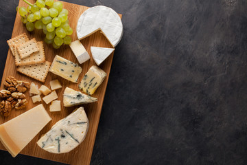 Tasting cheese dish on a wooden plate. Food for wine and romantic, cheese delicatessen on a dark stone table. Top view with copy space