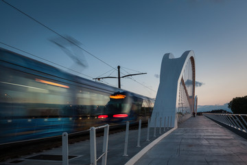 Fahrende Bahn mit sichtbarer Bewegungsgeschwindigkeit über die Beatus-Rhenanus-Brücke in Kehl zur blauen Stunde - obrazy, fototapety, plakaty
