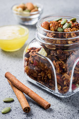 Pumpkin spice honey cinnamon granola in a glass jar with ingredients on concrete background. Selective focus, close up.