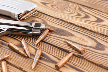 Single metal glossy pistol and silver magazine with scattered bullets for assault rifle on old rustic wooden weathered planks