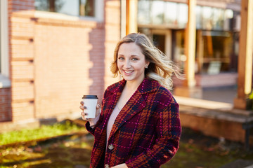 young blond woman smiling with coffee at golden hour walking