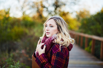 Naklejka premium young blond woman on bridge during autumn looking away grabbing scarf