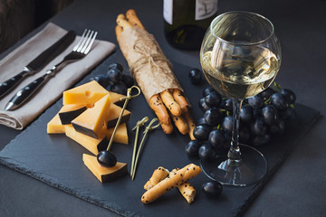Cheese plate served with crackers, grapes and glass of white wine on dark background.