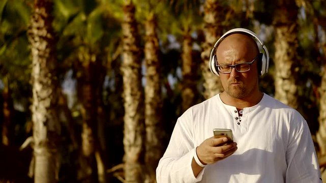 big, bald man with glasses and white shirt listening to your favorite music via wireless headphones. pure sound quality. modern technology for life and leisure
