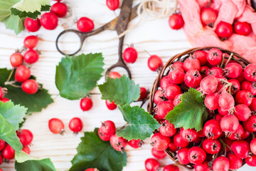 Berries and leaves of hawthorn in a wicker basket on a wooden table. Top view