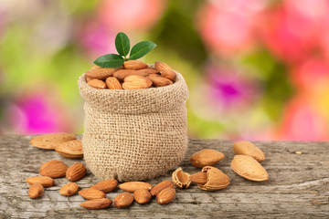 Almonds with leaf in bag from sacking on a wooden table with blurred garden background
