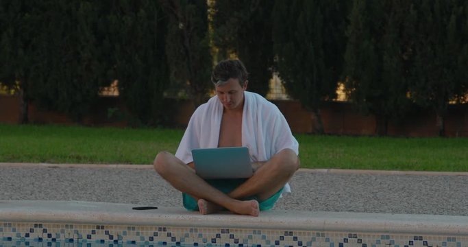 Happy businessman relaxing and having fun by country house. Freelancer uses laptop, near the swimming pool. The rich and successful Spanish businessman uses laptop in the yard, reflection in water