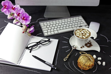 Female work space with computer, orchid, coffee and notebook with glasses and pen on black background. Morning breakfast on work place
