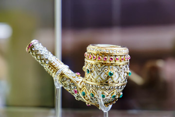 Ancient golden smoking pipe in precious stones on a stand. Selective focus