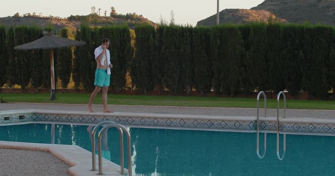 Happy businessman relaxing and having fun by country house. Freelancer uses laptop, near the swimming pool. Young and rich Spanish businessman talking on the phone in the pool